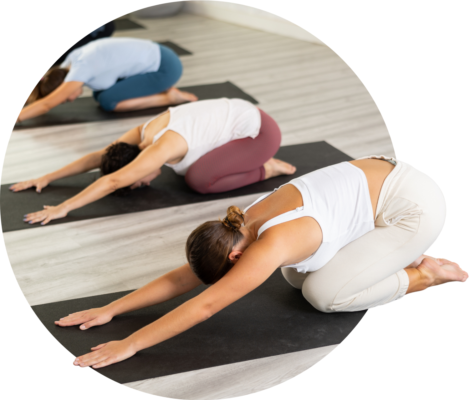 Women practicing yoga in a studio, performing a child’s pose on yoga mats, promoting wellness and fitness for gym memberships.
