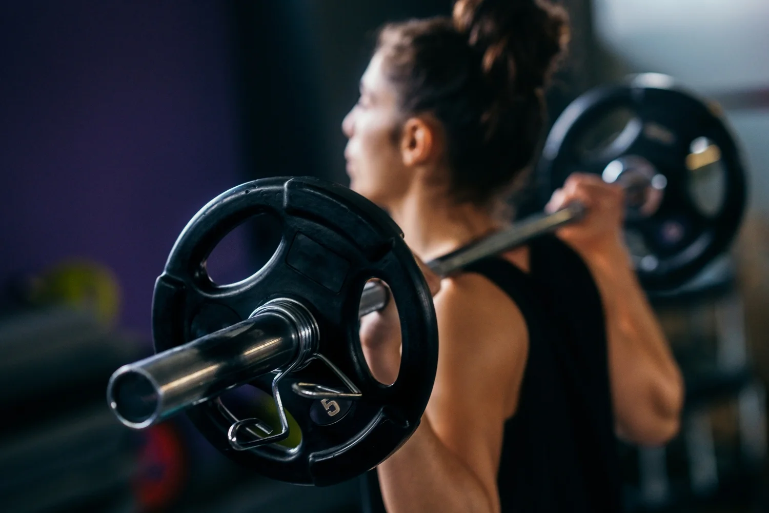 Woman lifting a barbell in a gym, emphasizing strength training and fitness, relevant to gym branding and marketing strategies.
